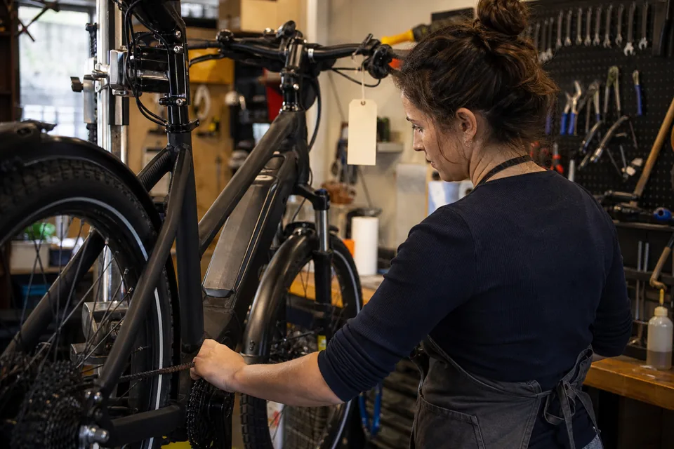 Mechanic in a bicycle shop service area tuning an electric bike while a work ticket hangs from the handlebar