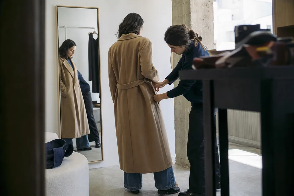 Associate helping a client choose a coat in a quiet fashion boutique fitting salon