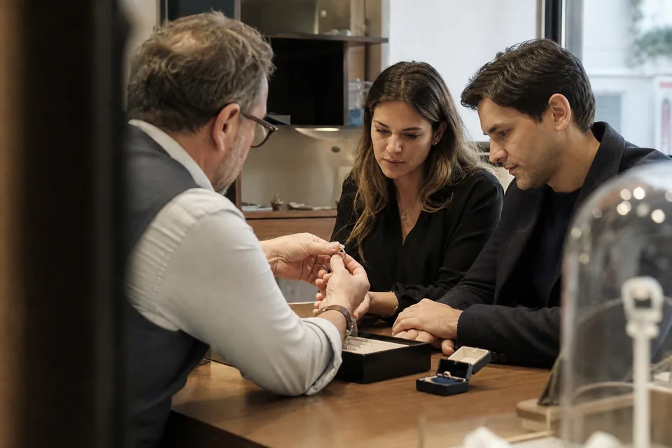 Jeweler showing a diamond ring to a client across a glass counter in a bright store