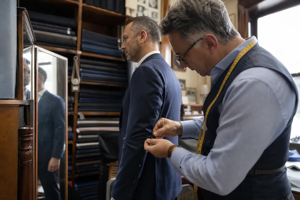 Custom clothier pinning the sleeve of a suit jacket on a client during a fitting in a tailor shop