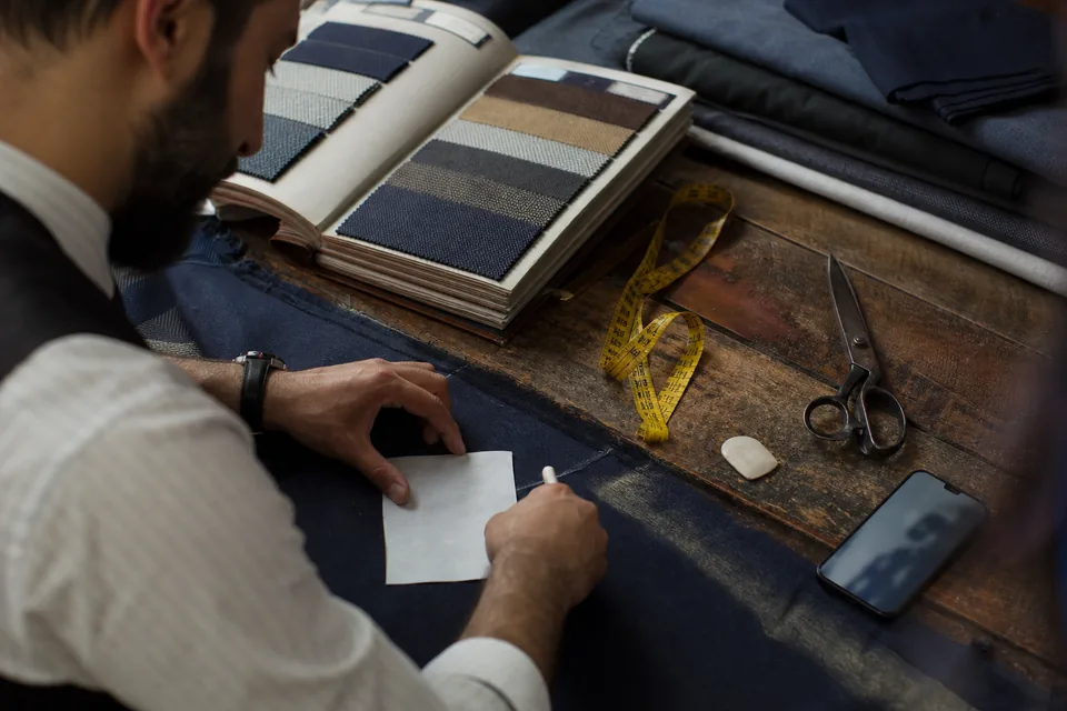 Paper measurement card, fabric swatch book and a phone on a tailor's cutting table