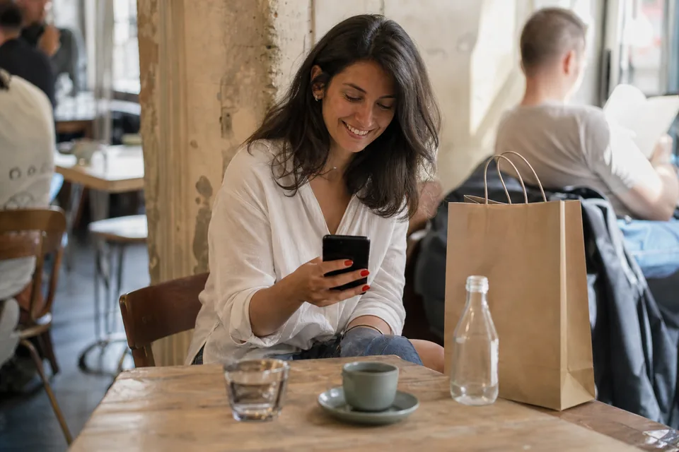 Client reading a personal message from her boutique on a phone in a sunlit cafe
